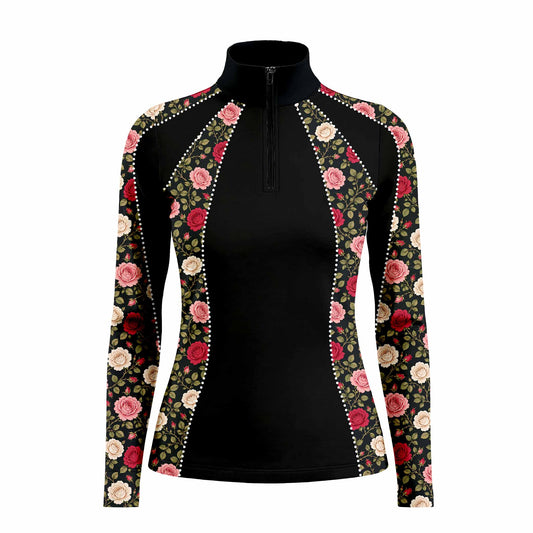 Lifestyle shot outside white stable farmhouse of female rider wearing black vintage rose floral long‑sleeve riding top with rhinestone‑dot panel trim, paired with beige riding breeches