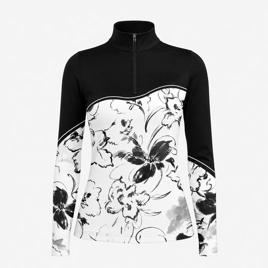 Sunny sandy paddock lifestyle shot of female equestrian beside grey horse, wearing black‑white color‑block ink‑wash floral print long‑sleeve riding top and black riding breeches