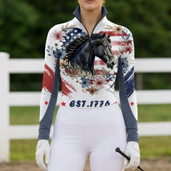 Model wearing the American Flag Floral Horse Print Riding Top at an outdoor equestrian arena, with jumps in the background