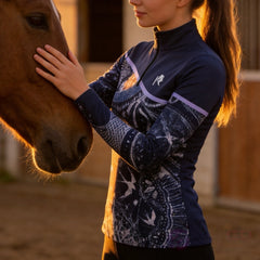 Model wearing the Celestial Night Print Color-Block Riding Top petting a horse in a sunlit stable