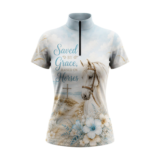 Full-body model shot wearing serene beach floral cross horse short sleeve top at outdoor equestrian show jumping arena with spectator stands, holding riding crop