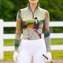 Model wearing the Equestrian Portrait Oil Painting Print Long-Sleeve Riding Top at an outdoor equestrian arena, with jumps in the background
