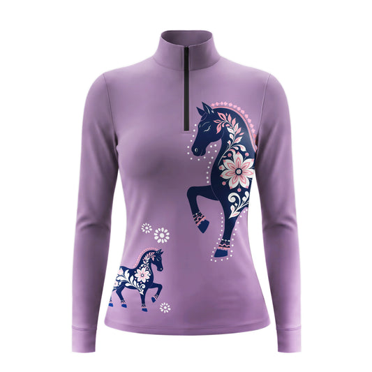 Full-body model shot wearing soft pastel folk floral horse long sleeve top at sunlit green pasture white wooden fence, holding riding crop