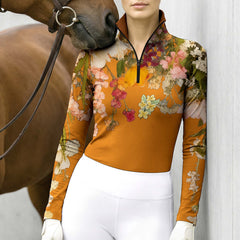 Model wearing mustard floral riding top beside brown horse leaning against grey wall