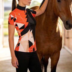 Sunlit indoor stable side shot of model touching brown horse showcasing bold abstract geometric horse print equestrian short sleeve top
