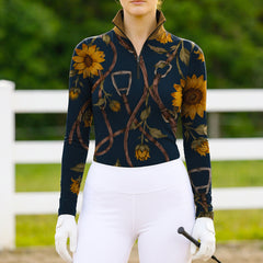 Model wearing vibrant sunflower riding top at sunlit green pasture fence