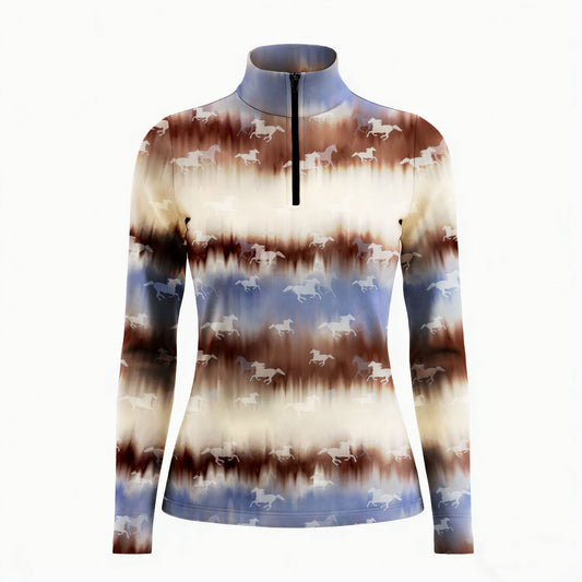 Smiling model sitting on weathered wooden ranch fence bench wearing muted western tie-dye horse silhouette long sleeve riding top in golden pasture light