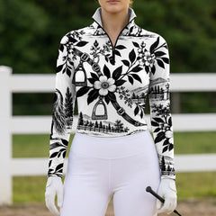 Front view of the printed riding top worn by a rider holding a riding crop near a white pasture fence