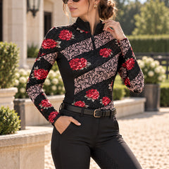 Rider in the floral riding top adjusting her collar while standing on a gravel stable yard