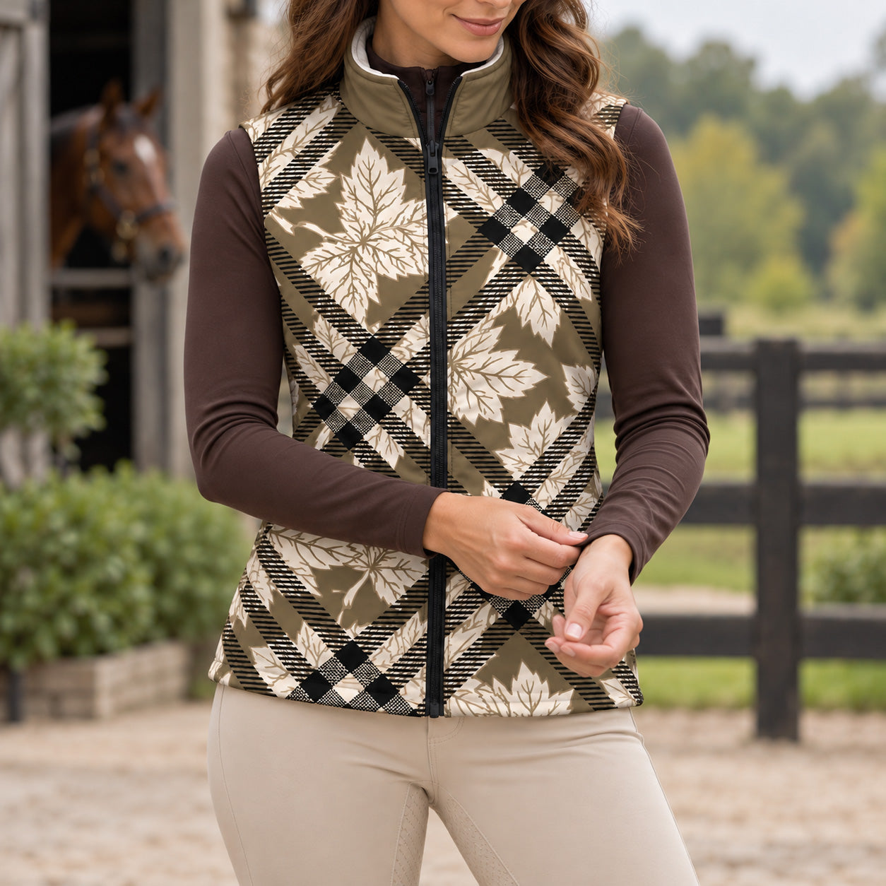 Olive toned maple leaf and plaid print side of reversible vest worn with beige riding breeches and tall boots near horses in stable stalls