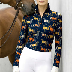 Navy blue horse print long sleeve quarter zip riding top styled with white breeches and white gloves, next to a brown horse with a leather bridle against a white wall