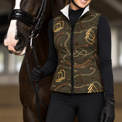 Woman wearing the olive stirrup and chain print side of the reversible quilted vest over a black long sleeve base layer with black breeches and gloves beside a dark bay horse