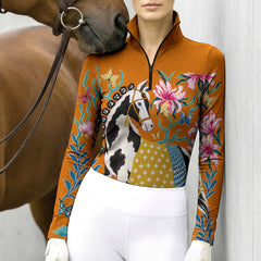 Close view of the orange riding top showing the pinto horse print, floral details, butterflies, standing collar, and quarter zip front