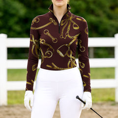 Woman wearing burgundy equestrian tack print quarter-zip top at farm fence