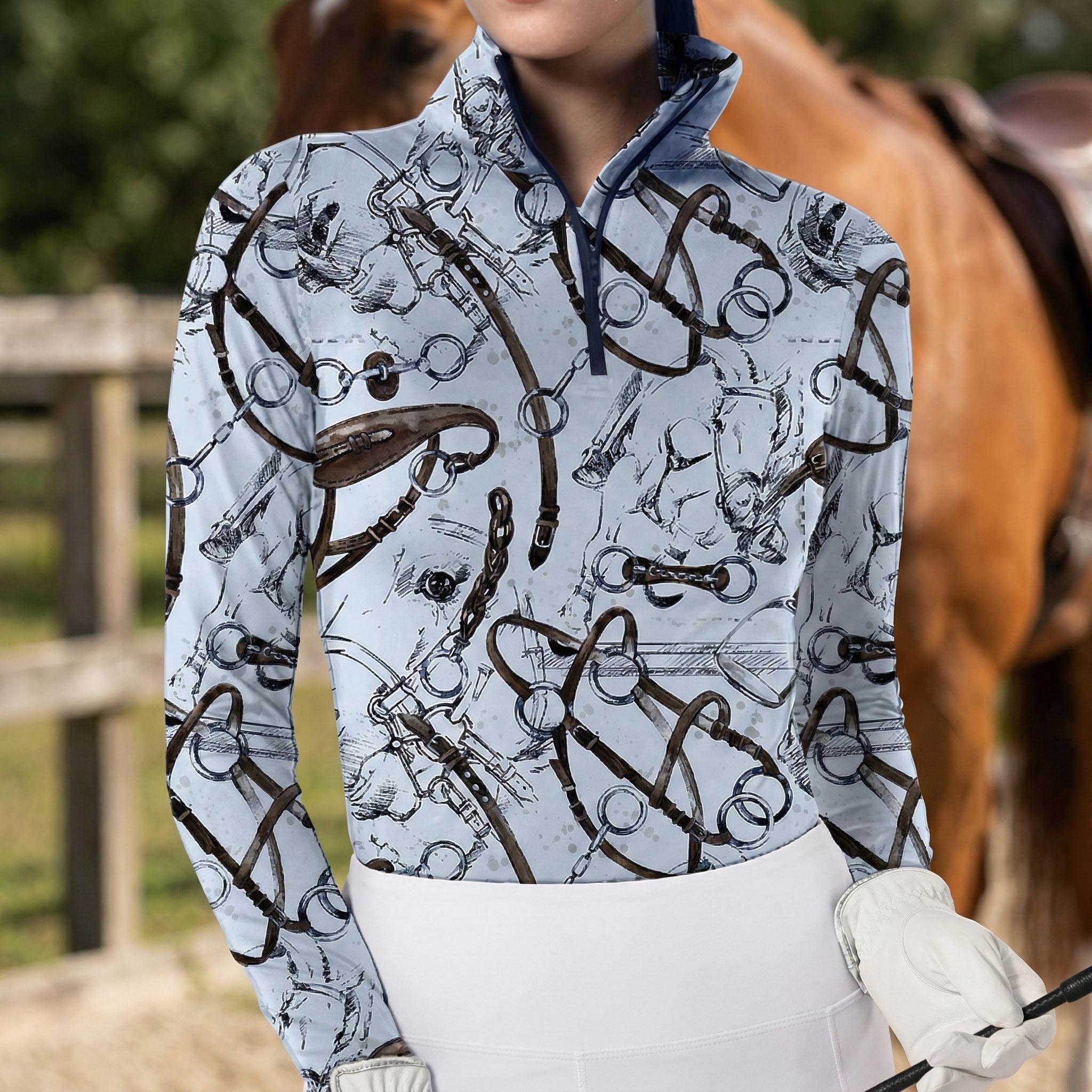 Woman wearing light blue equestrian tack sketch print long sleeve zip top standing beside a horse at the stable