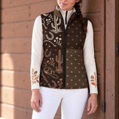 Woman wearing a brown reversible quilted vest with cream and tan western artwork on the right front panel and light diamond shapes on the left front panel