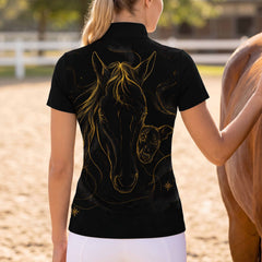 Back‑view outdoor arena shot of female rider next to brown horse showing full back golden horse‑whippet celestial‑star sketch print on black short‑sleeve riding top