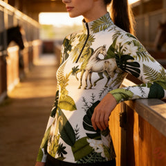 Sunset stable aisle lifestyle shot of female equestrian wearing tropical foliage vintage horse all‑over‑print long‑sleeve riding top