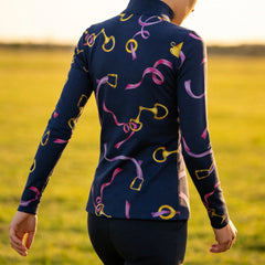Outdoor field back‑view lifestyle shot of women’s navy‑base long‑sleeve quarter‑zip riding top with golden bit buckle and pink purple ribbon all‑over print