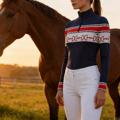 Golden sunset paddock outdoor lifestyle shot of female equestrian beside chestnut horse wearing navy red‑white horse‑bit stripe long‑sleeve quarter‑zip riding top