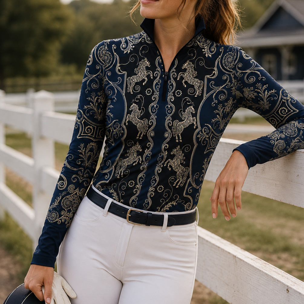 Close‑up show arena shot of equestrian model in navy‑black all‑over golden carousel‑horse scroll‑filigree print long‑sleeve quarter‑zip riding top, matched with clean white breeches and white riding gloves