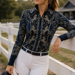 Close‑up show arena shot of equestrian model in navy‑black all‑over golden carousel‑horse scroll‑filigree print long‑sleeve quarter‑zip riding top, matched with clean white breeches and white riding gloves