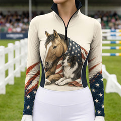 Outdoor show‑arena lifestyle shot of female equestrian wearing cream long‑sleeve riding top with horse border collie USA flag themed front graphic