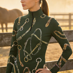 Outdoor golden‑hour pasture fence lifestyle shot of female equestrian wearing forest‑green long‑sleeve quarter‑zip riding top with watercolor horse‑tack all‑over print