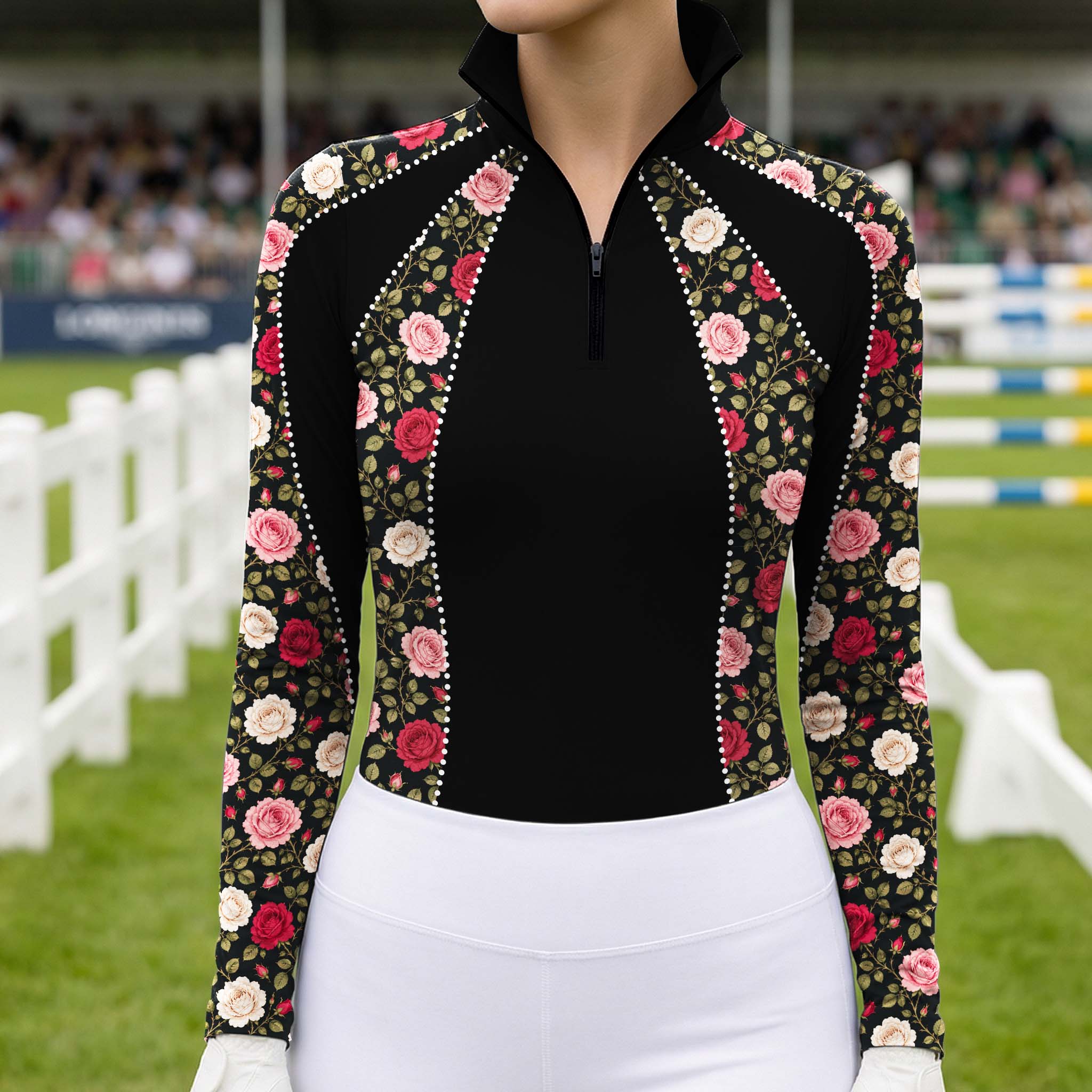 Outdoor equestrian show arena shot of female rider wearing black vintage rose floral rhinestone‑trim long‑sleeve riding top, paired with white breeches and white riding gloves