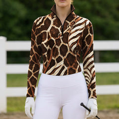 Outdoor paddock white‑fence lifestyle shot of female rider in safari giraffe‑zebra bridle‑harness print long‑sleeve riding top paired with white riding breeches and white riding gloves