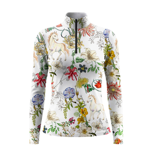 Garden ranch lifestyle shot of female equestrian seated beside brown horse, wearing cream watercolor wildflower and white unicorn‑pony print long‑sleeve riding top, white breeches and brown leather belt
