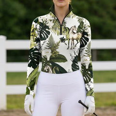 Outdoor pasture fence lifestyle shot of female rider wearing tropical botanical horse‑print long‑sleeve riding top paired with white breeches