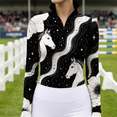 Rider standing at equestrian show jumping grounds wearing black cosmic galaxy horse‑floral print long‑sleeve riding top
