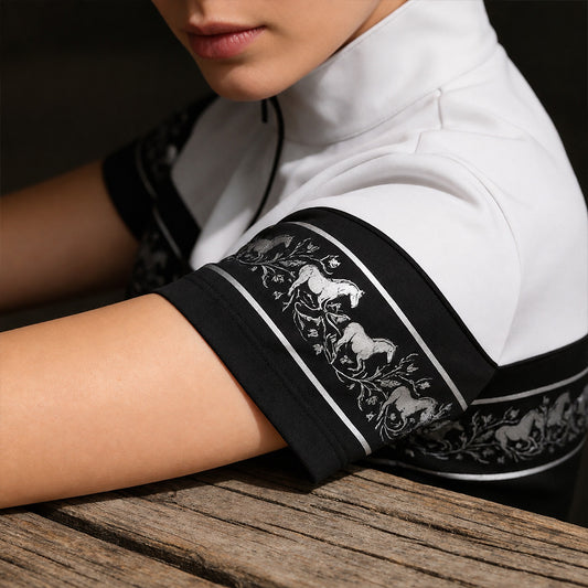 Close‑up studio shot focusing on sleeve border print details of black‑white galloping horse floral border short‑sleeve quarter‑zip riding top resting on wooden table