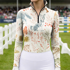 Equestrian show‑ground close‑up shot of rider in cream pastoral horse‑dog botanical print long‑sleeve riding top, paired with white breeches and riding gloves
