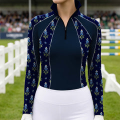 Outdoor equestrian show arena shot of female rider wearing navy bluebonnet print rhinestone‑trim long‑sleeve riding top, paired with white breeches and white riding gloves