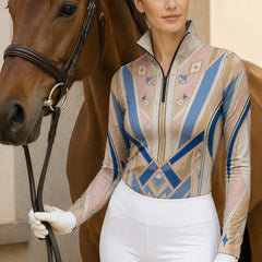 Outdoor lifestyle shot of female equestrian holding horse reins beside brown horse wearing blush‑blue art‑deco geometric star long‑sleeve riding top