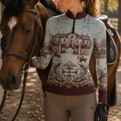 Paddock lifestyle close‑up shot of female equestrian touching brown horse’s face wearing burgundy‑trim French chateau blueprint print long‑sleeve riding top and taupe breeches