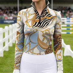 Lifestyle shot with brown horse nuzzling rider’s shoulder, female equestrian leans against light wall in cream equestrian tack zebra leopard print riding top and white riding gloves