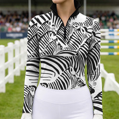 Equestrian showground competition arena lifestyle shot of female rider wearing black‑white zebra‑head collage print long‑sleeve riding top and white riding breeches