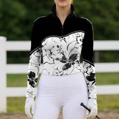 Green pasture fence front‑view lifestyle shot of female equestrian holding riding crop, wearing black‑white color‑block ink‑wash floral print long‑sleeve riding top and white breeches