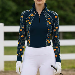 Outdoor pasture fence‑side lifestyle shot of female rider in navy golden california poppy floral print long‑sleeve riding top