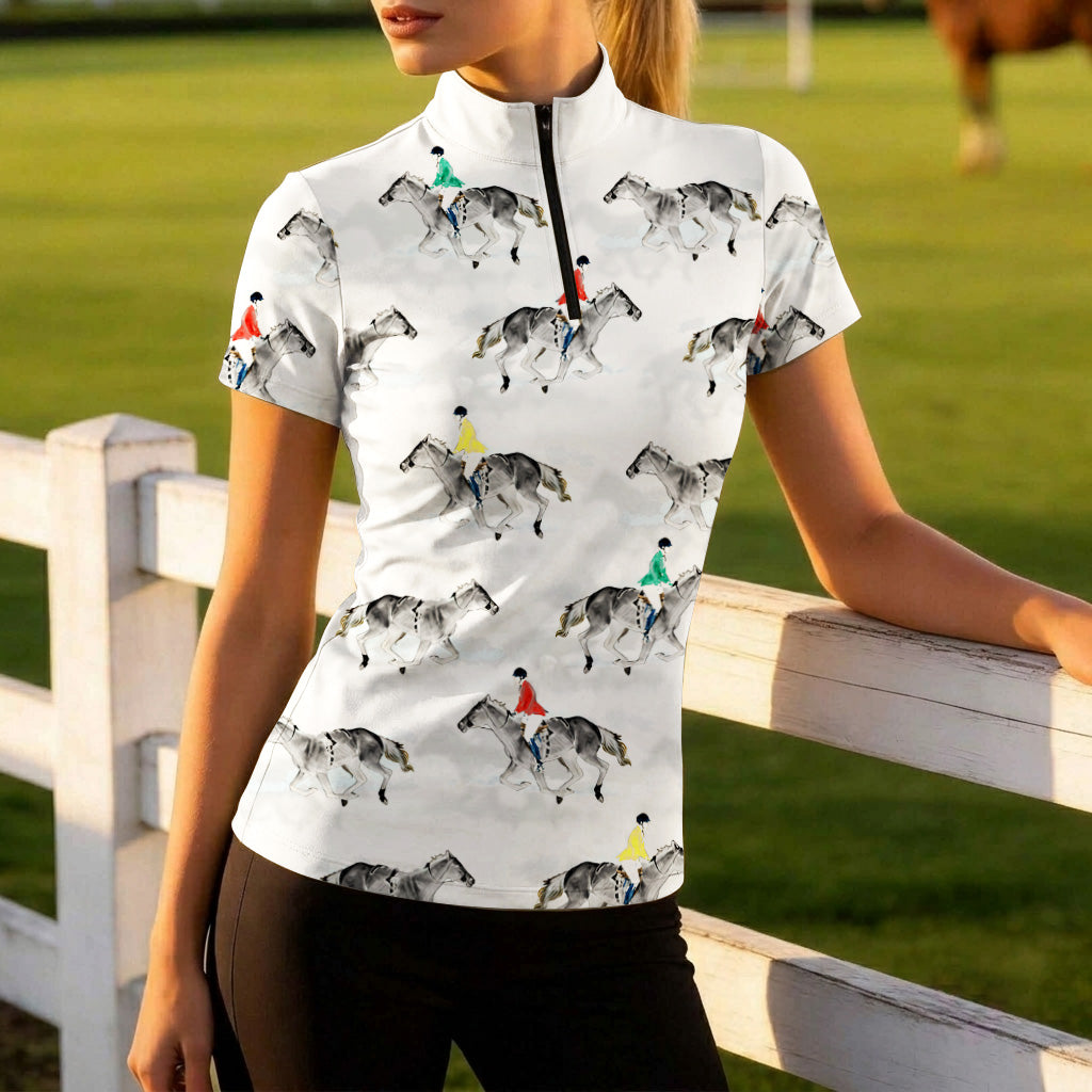 Golden‑hour green pasture lifestyle shot of female equestrian leaning on white wooden fence wearing white short‑sleeve riding top with watercolor jumping rider all‑over print