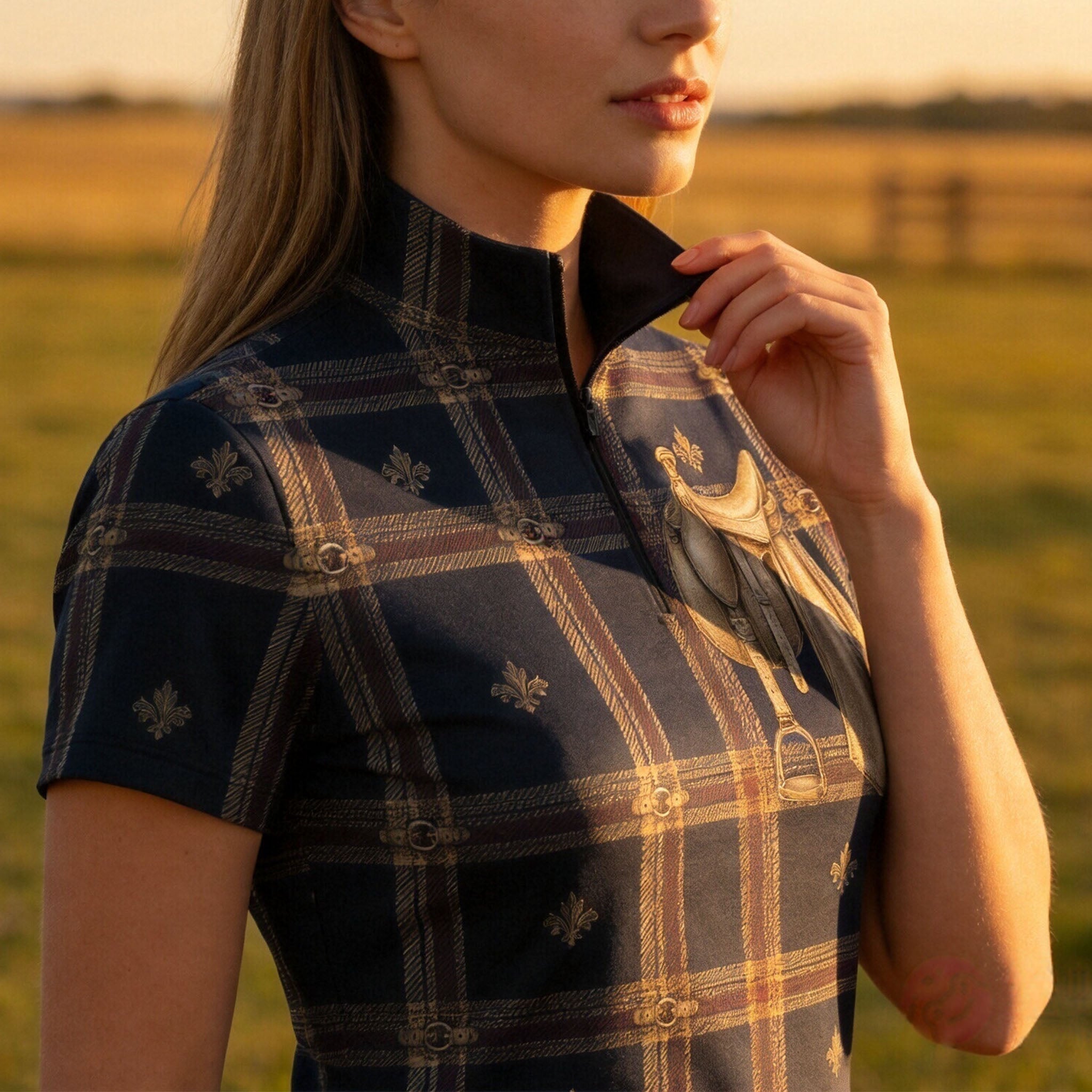 Golden hour rural field close‑up shot of female equestrian adjusting collar on navy tartan saddle‑print riding top