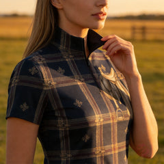 Golden hour rural field close‑up shot of female equestrian adjusting collar on navy tartan saddle‑print riding top