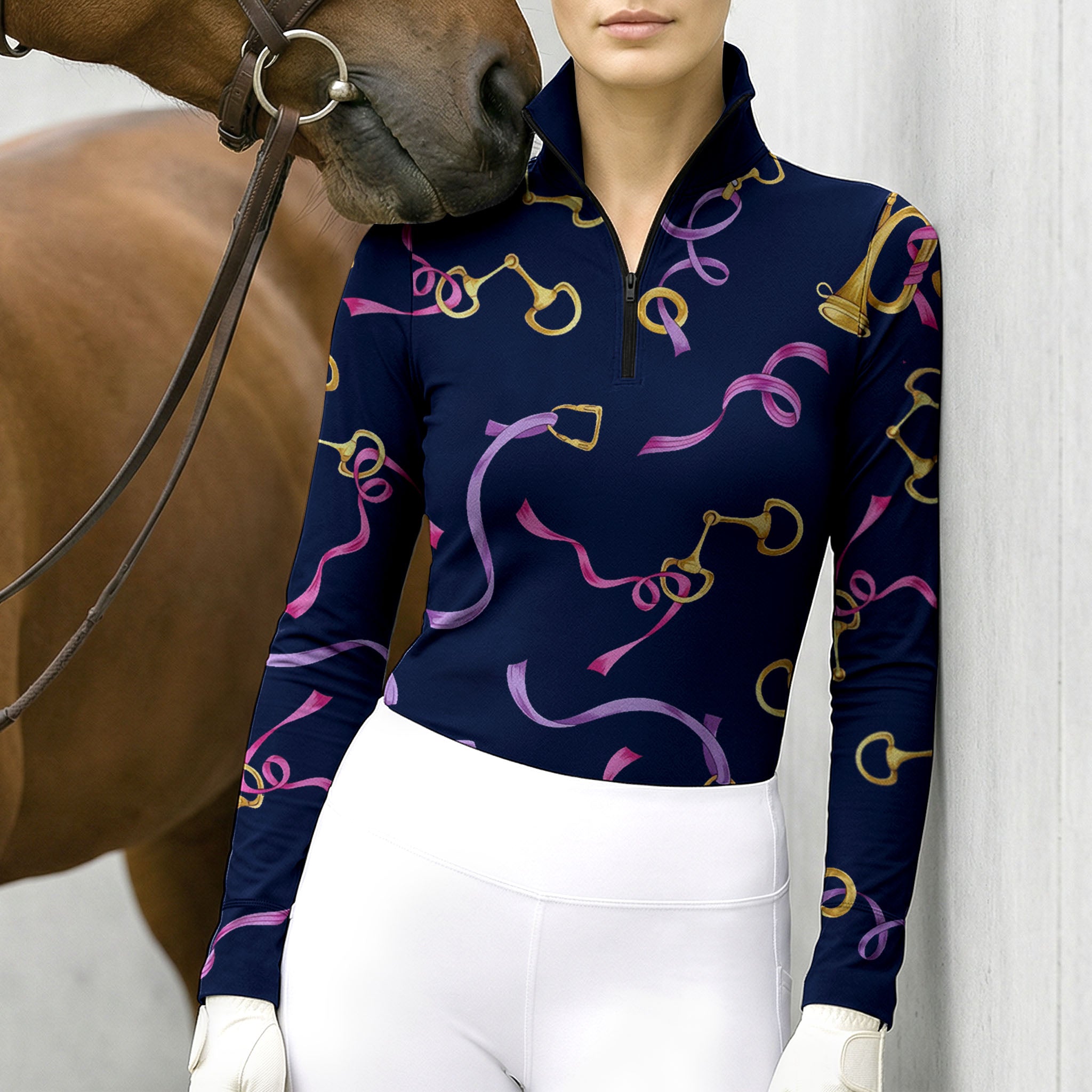 Stable‑wall lifestyle shot of female equestrian beside horse wearing navy‑base long‑sleeve riding top with golden bit buckle and pink purple ribbon all‑over print