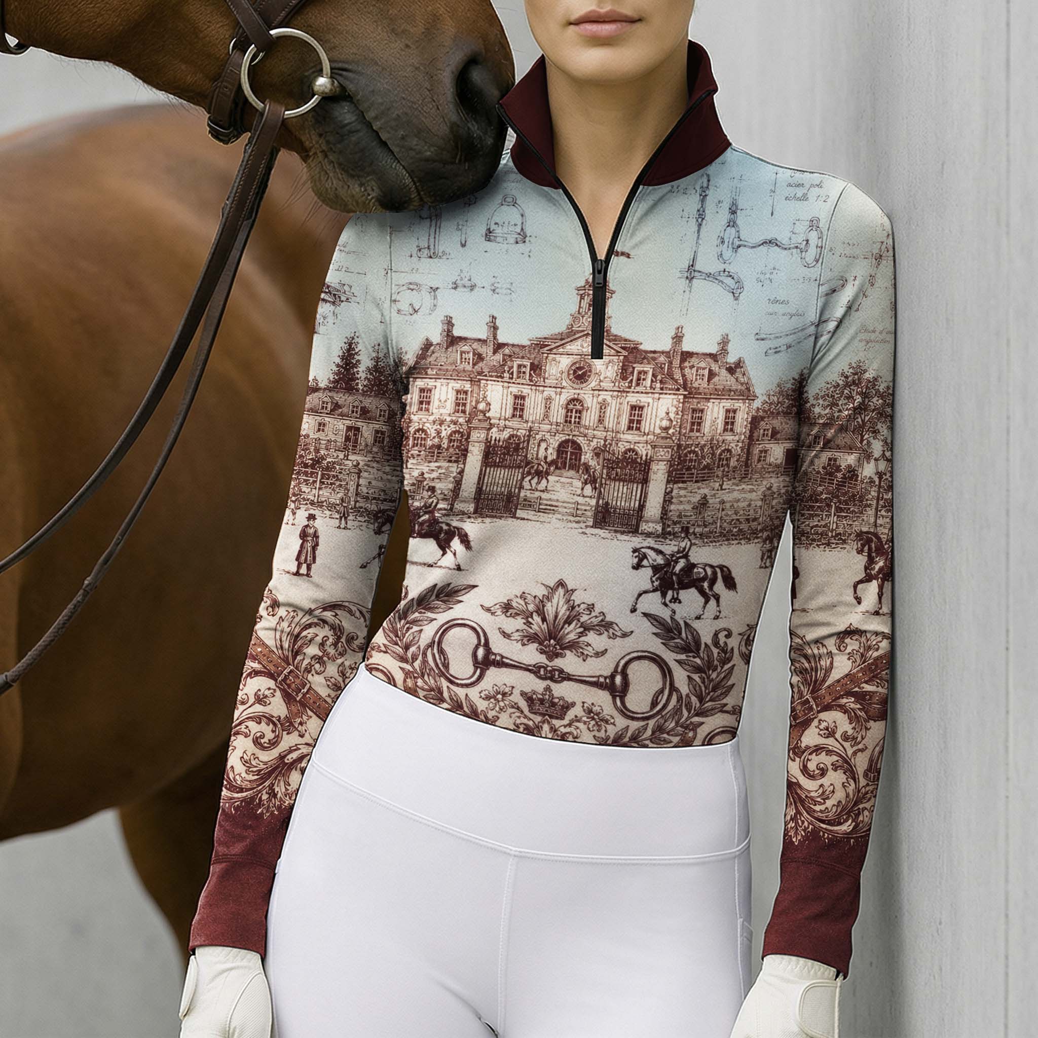 Neutral stone wall lifestyle shot of female equestrian as brown horse nuzzles her shoulder, wearing burgundy‑trim French chateau blueprint‑print long‑sleeve riding top and white breeches
