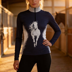 Golden‑hour stable aisle lifestyle shot of female rider wearing navy splash‑effect galloping‑horse long‑sleeve riding top