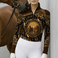 Stable yard lifestyle shot of female rider wearing cream‑black ink‑wash floral long‑sleeve riding top, paired with white breeches and white riding gloves beside wooden fence