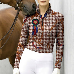 Show ground fence portrait lifestyle shot of female rider leaning on white wooden fence, wearing charcoal equestrian tack zebra leopard mixed‑print long‑sleeve riding top, white breeches and white riding gloves